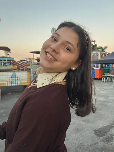 Duda Tiezzi sorrindo ao ar livre no fim da tarde