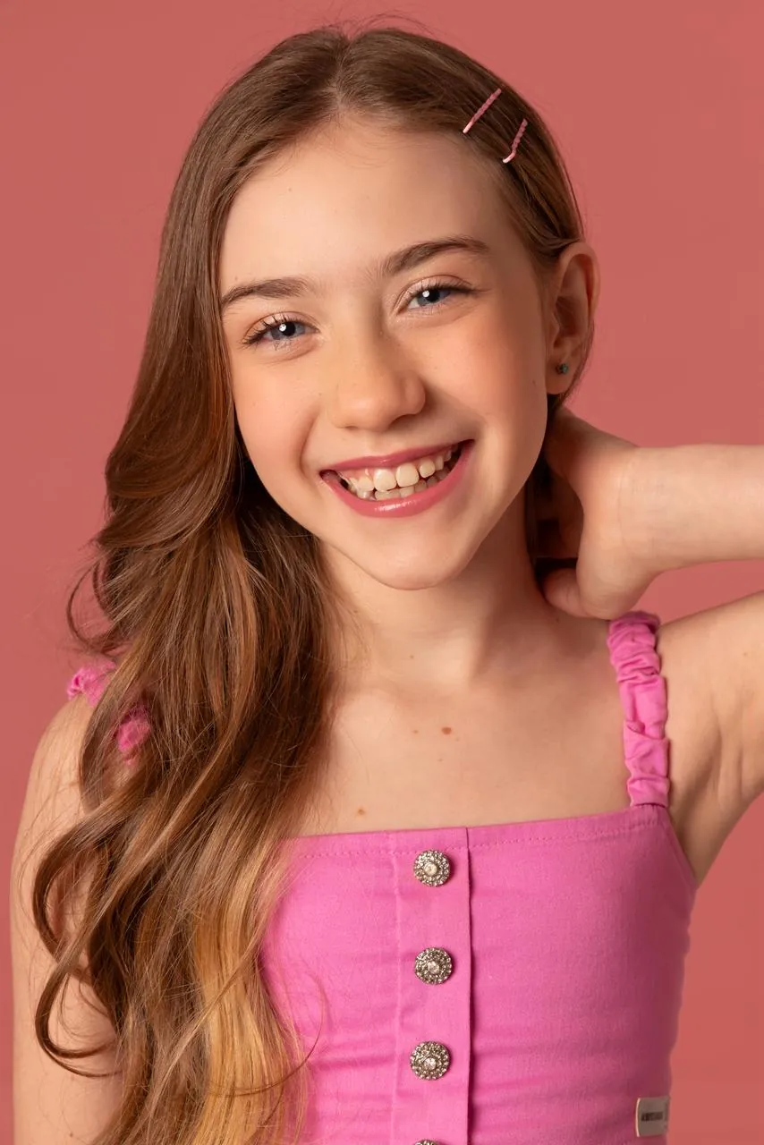 Isadora Lobregati sorrindo, de blusa rosa sobre fundo rosado