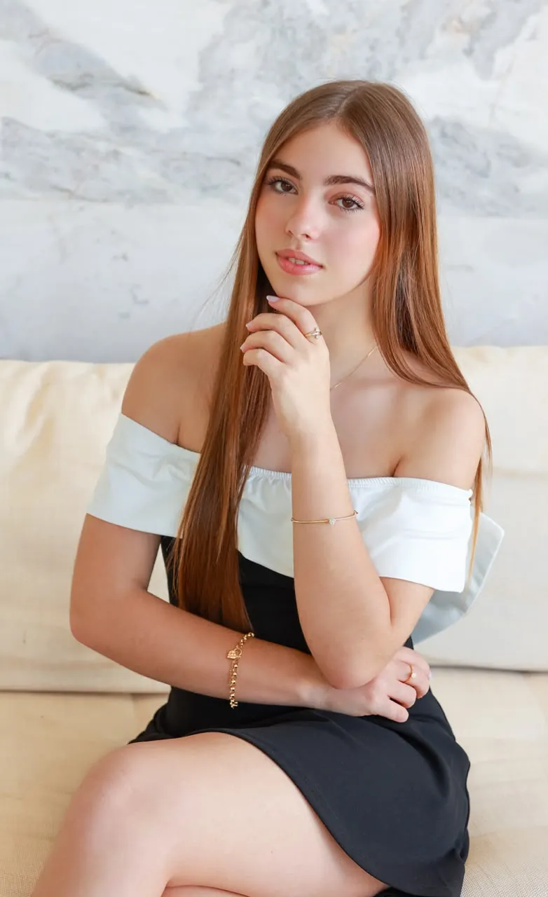 Maju Boaventura sentada em um sofá claro, com a mão no queixo